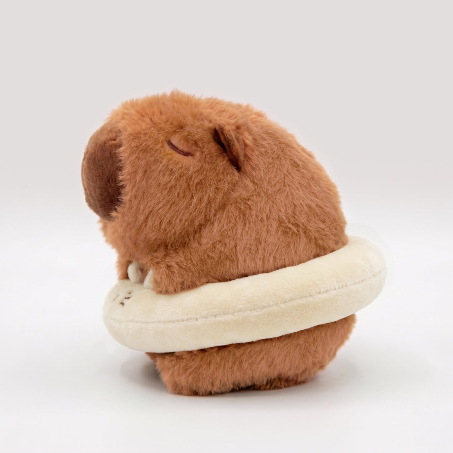 Side view of soft capybara plush wearing a cream floatie ring
