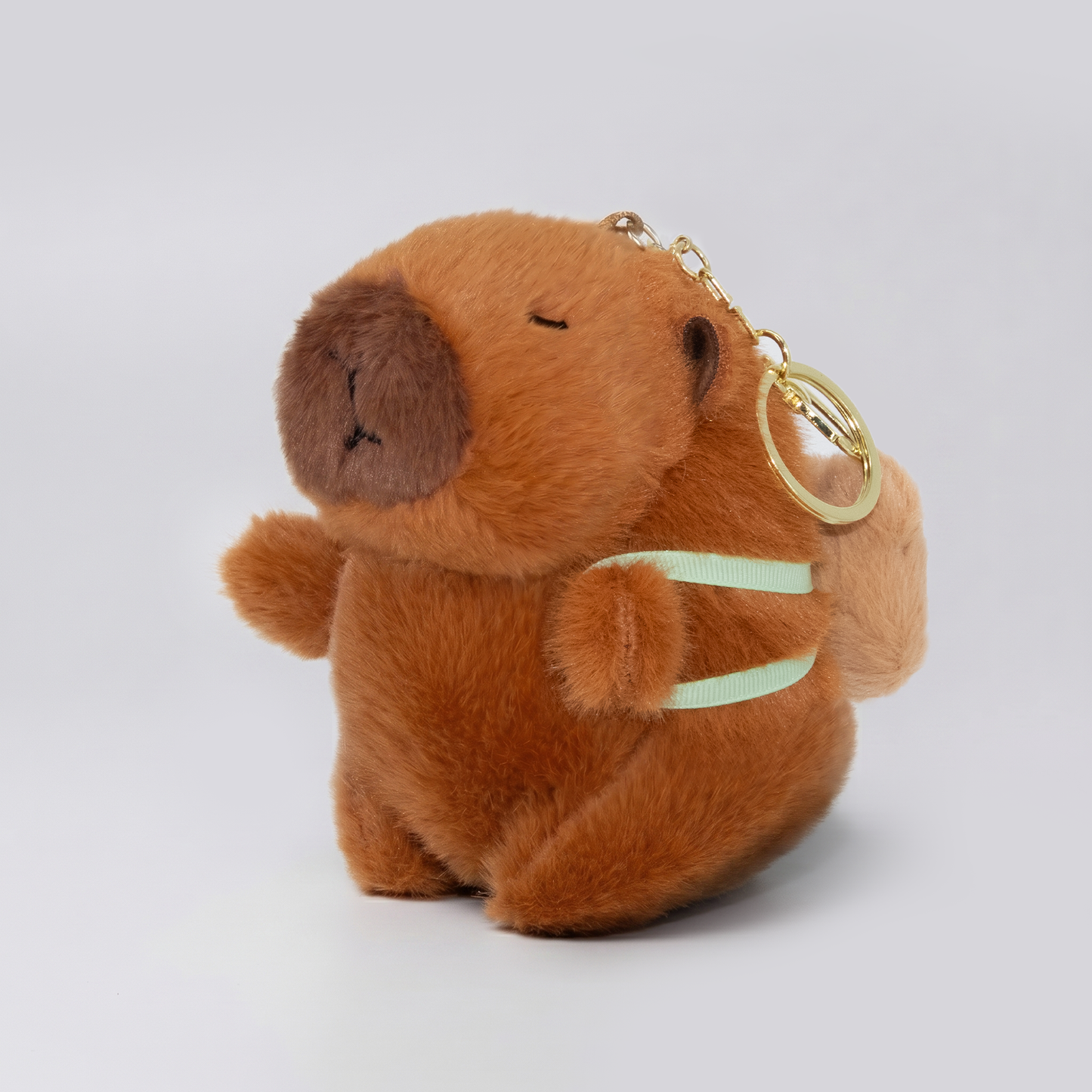 Soft capybara plush keychain wearing backpack with a gold keychain