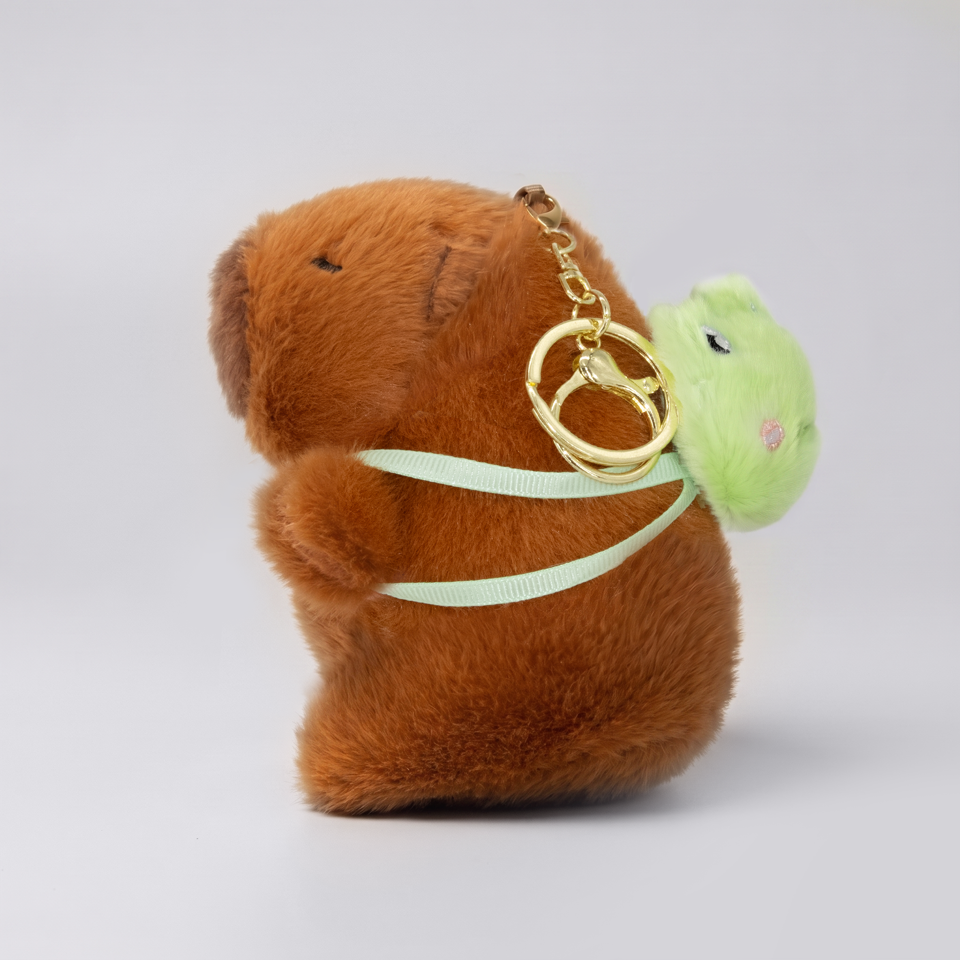 Soft capybara keychain wearing green frog shaped backpack with a gold keychain