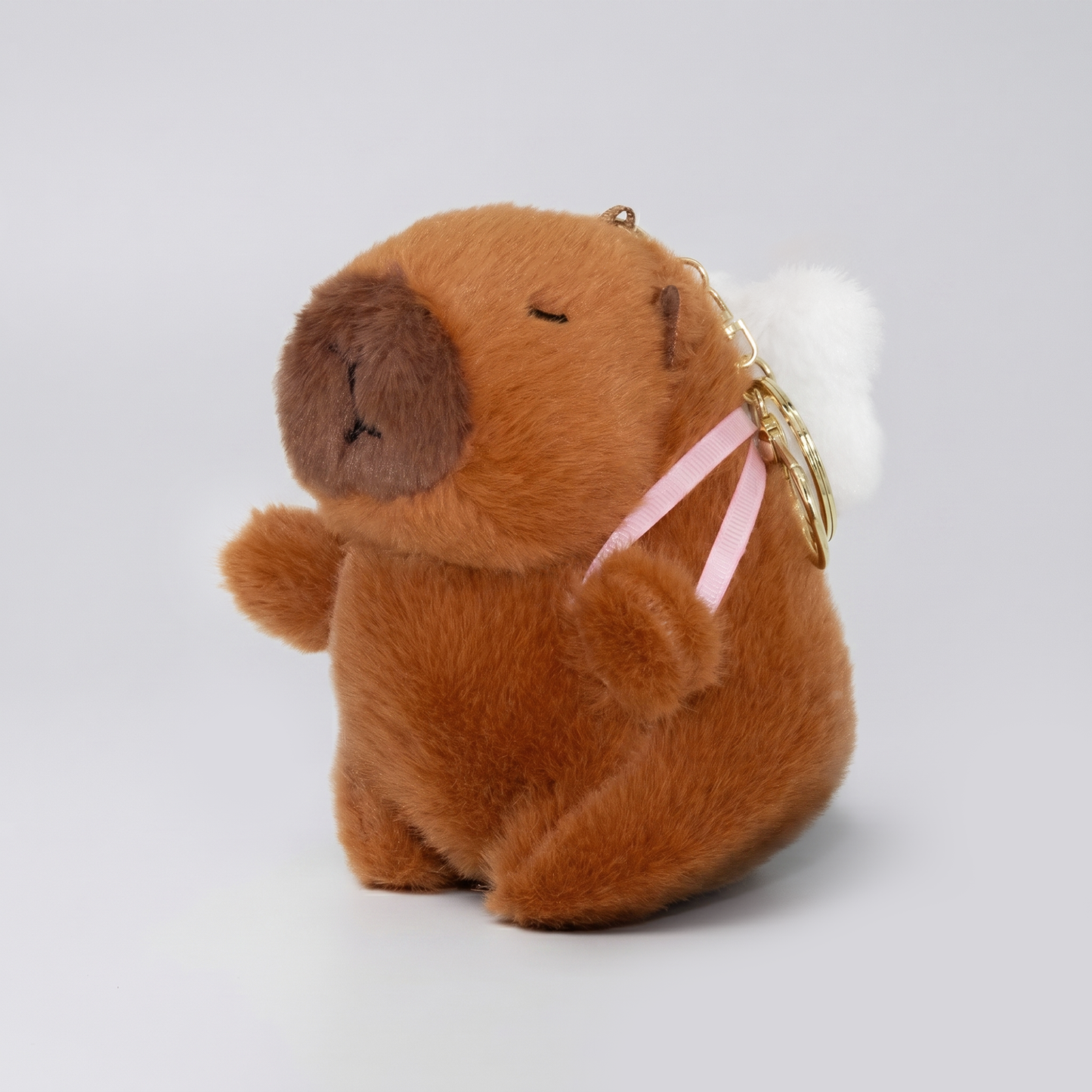 Soft capybara plush keychain wearing a panda plush shaped backpack with pink straps and a gold keyring keychain