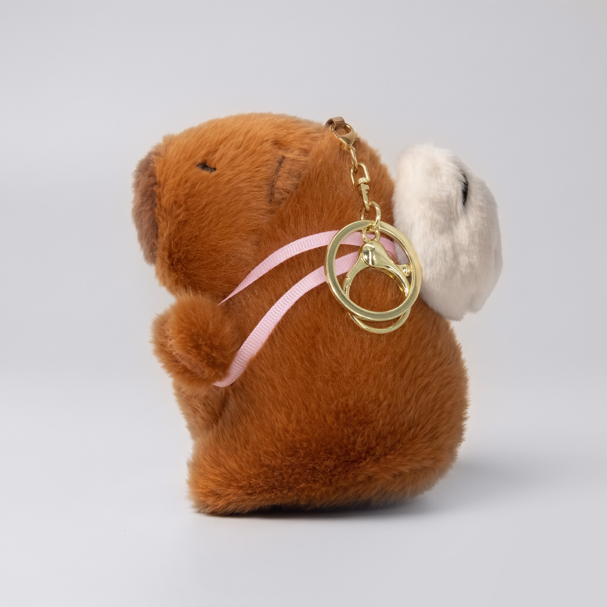 Soft capybara plush keychain wearing a panda plush shaped backpack with pink straps and a gold keyring keychain