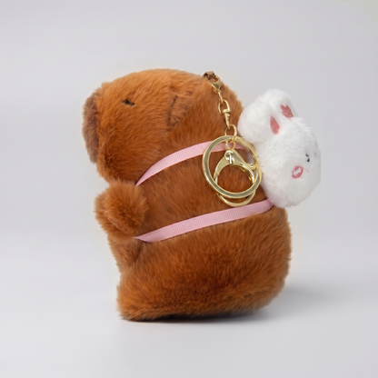 Soft capybara plush keychain wearing a rabbit plush shaped backpack with pink straps and a gold keyring keychain 