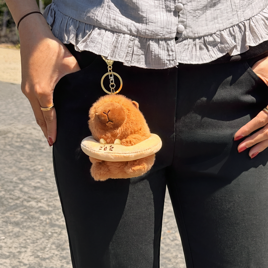 Cute brown capybara plush keychain wearing a cream floatie ring with a gold ring keychain clipped to a belt loop