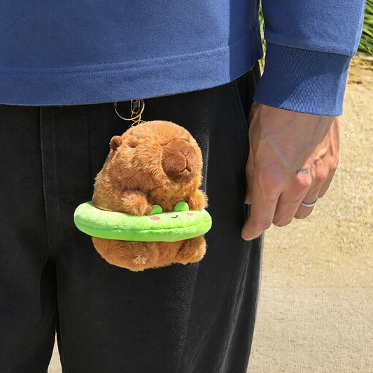 Capybara plush keychain wearing a bright green plush floatie with a frog face and gold keychain hanging from pants 