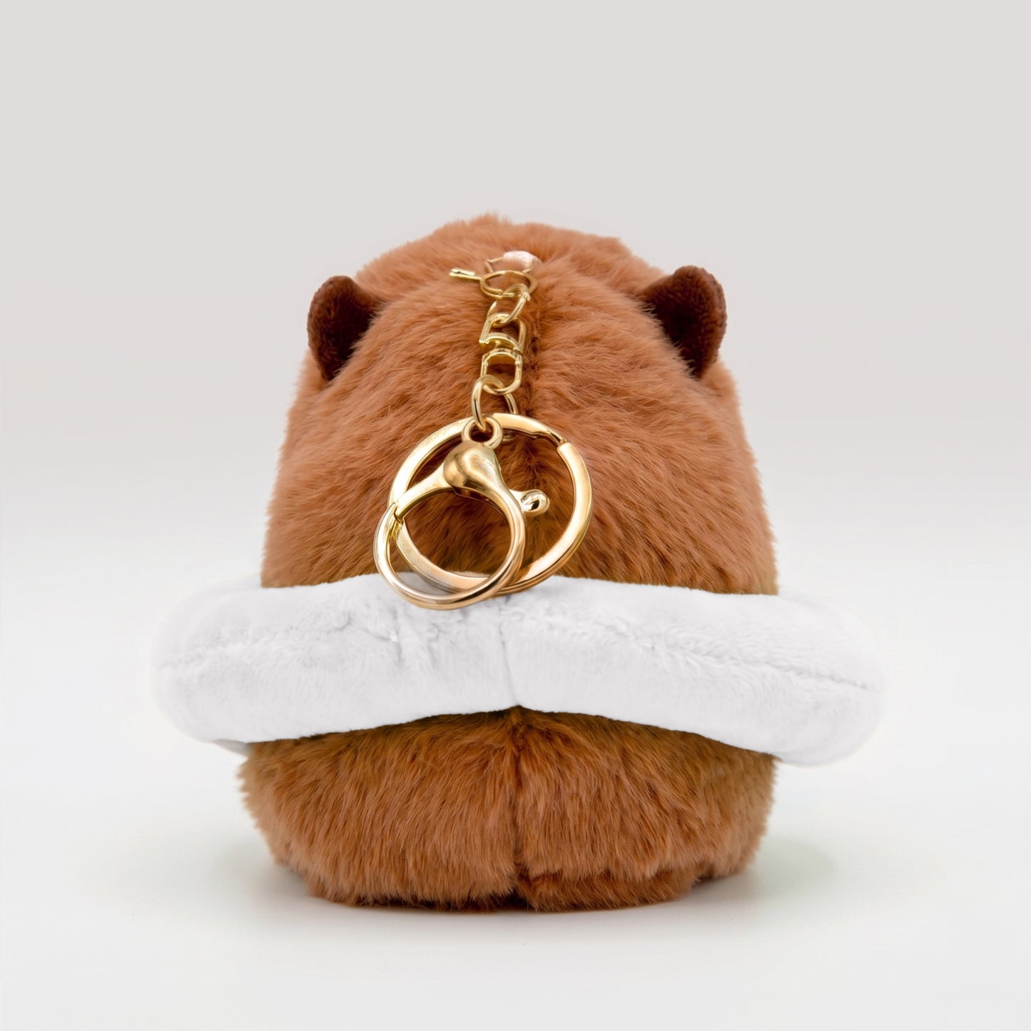 Back view of soft capybara plush wearing a white plush floatie with a gold keyring keychain on a white background