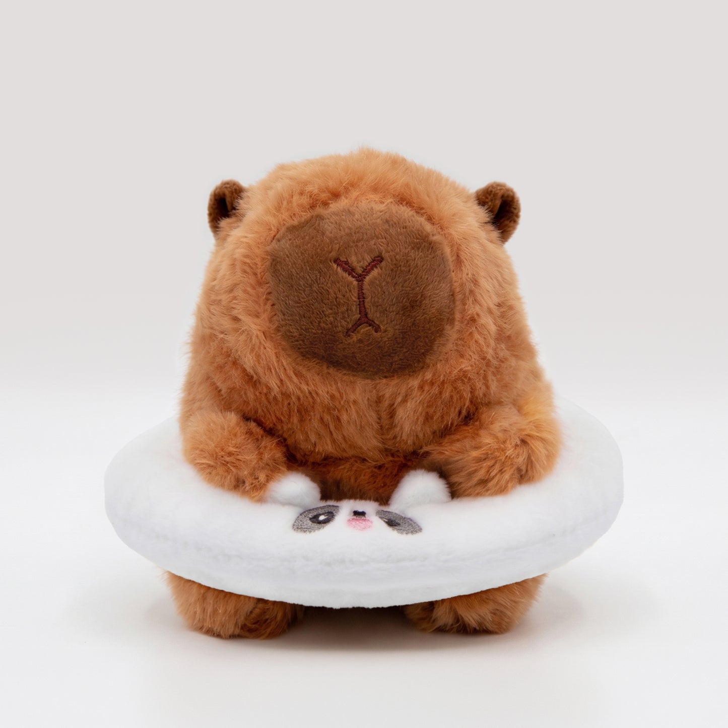 Soft capybara plush wearing a white plush floatie with a panda face on a white background