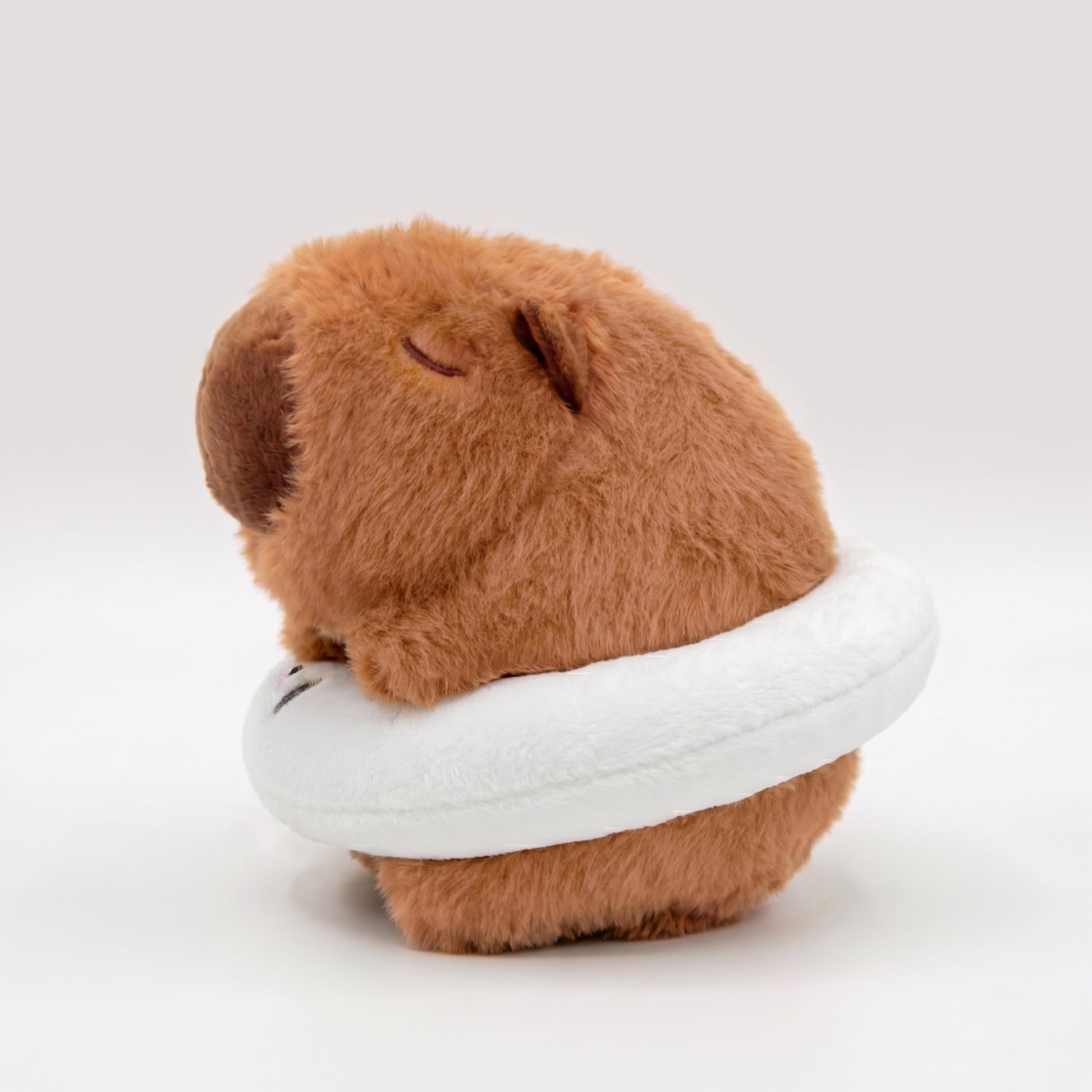 Soft capybara plush wearing a white plush floatie with a panda face on a white background