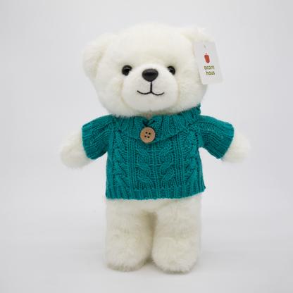 White teddy bear standing upright wearing a teal sweater with single button on a white background