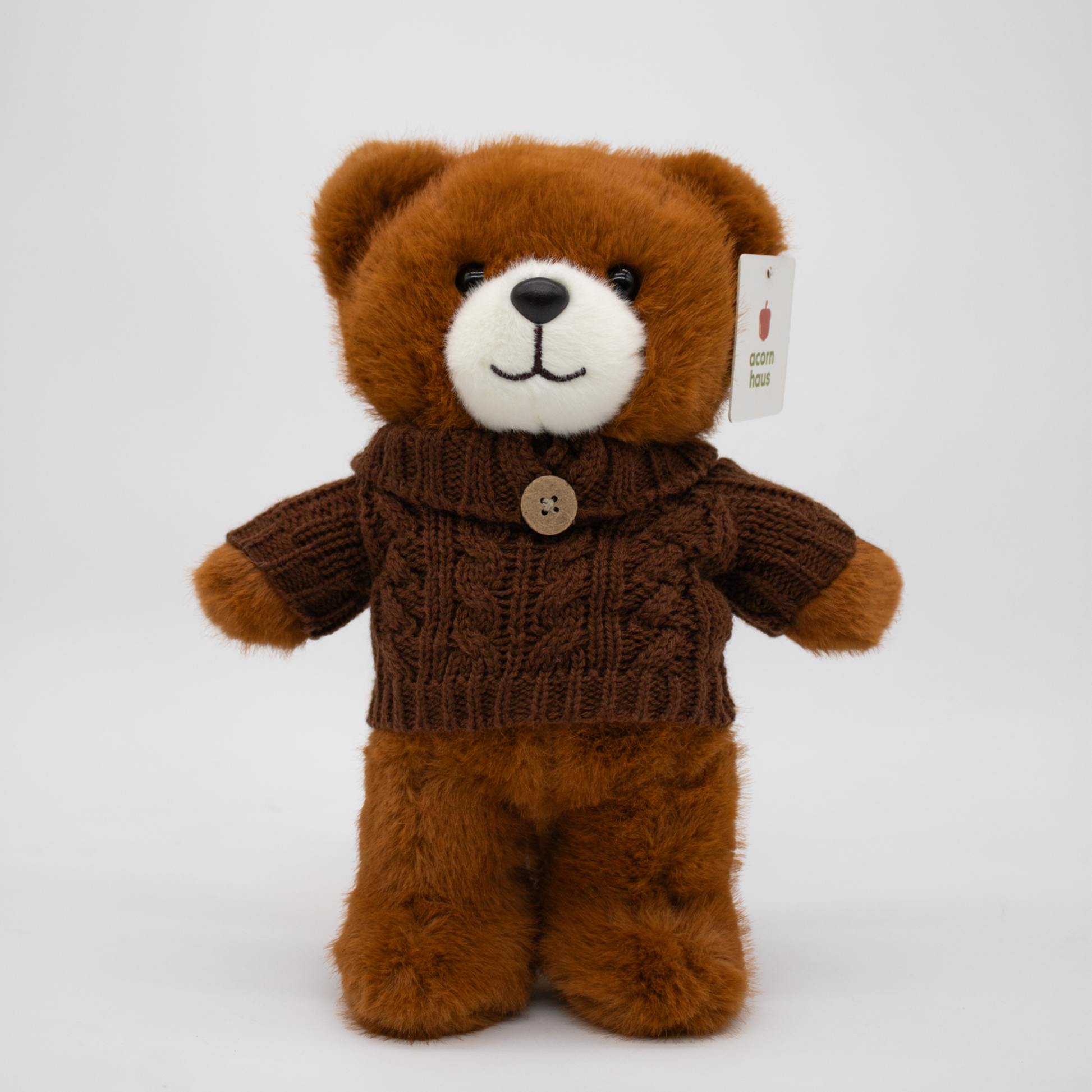 Brown Carrington teddy bear standing upright wearing a knitted sweater with a button on a white background