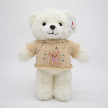 White Carrington teddy bear standing upright wearing a beige sweater with a brown bear wearing pink bow design on a white background