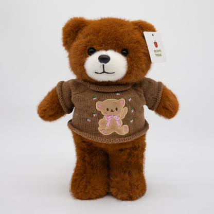 Brown Carrington teddy bear standing upright wearing a beige sweater with a brown bear wearing pink bow design on a white background