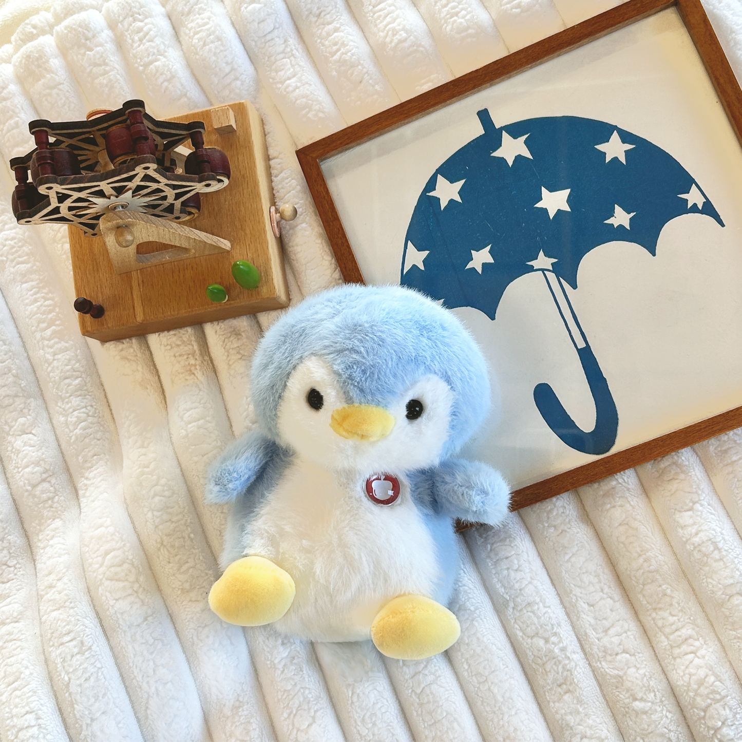 Plush penguin on a textured surface with a framed picture of an umbrella in the background