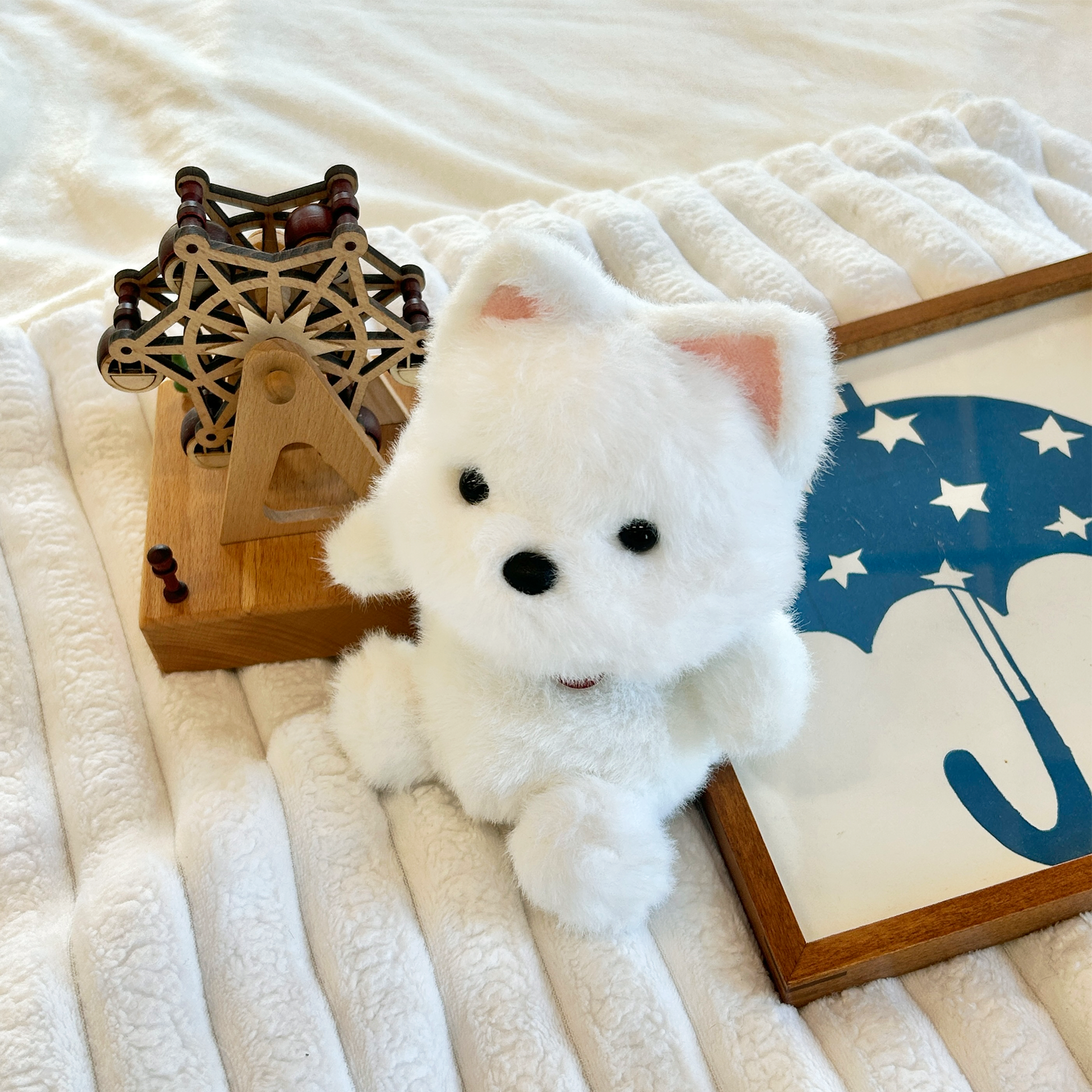 White plush puppy on a white blanket with wooden frame decorations on textured fabric blanket