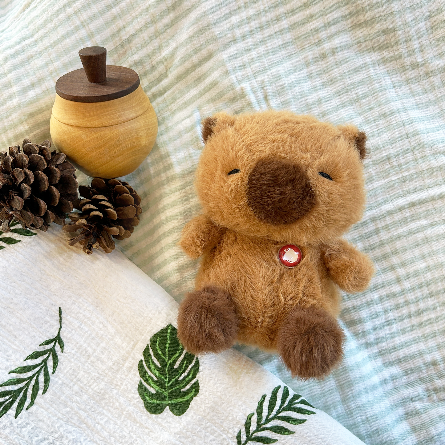 Plush capybara with wooden acorn and pinecones on a textured fabric background