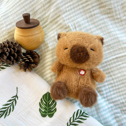 Plush capybara with wooden acorn and pinecones on a textured fabric background