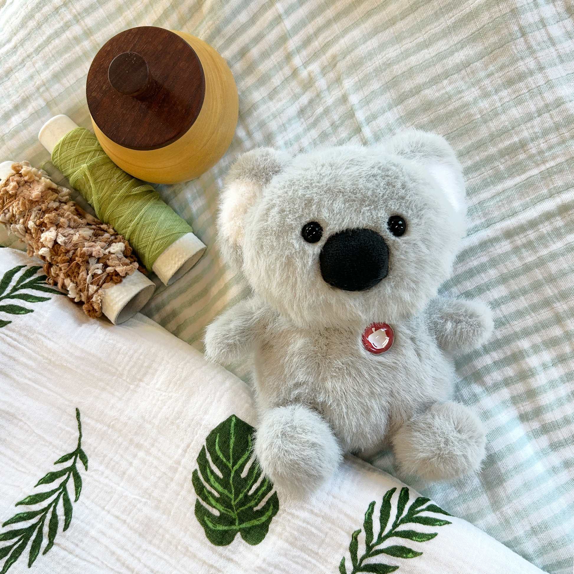 Plush koala with wooden acorn and spools on a textured blanket