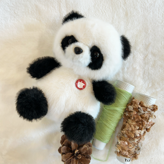 Plush panda with a spool of green thread and a pine cone on a white background