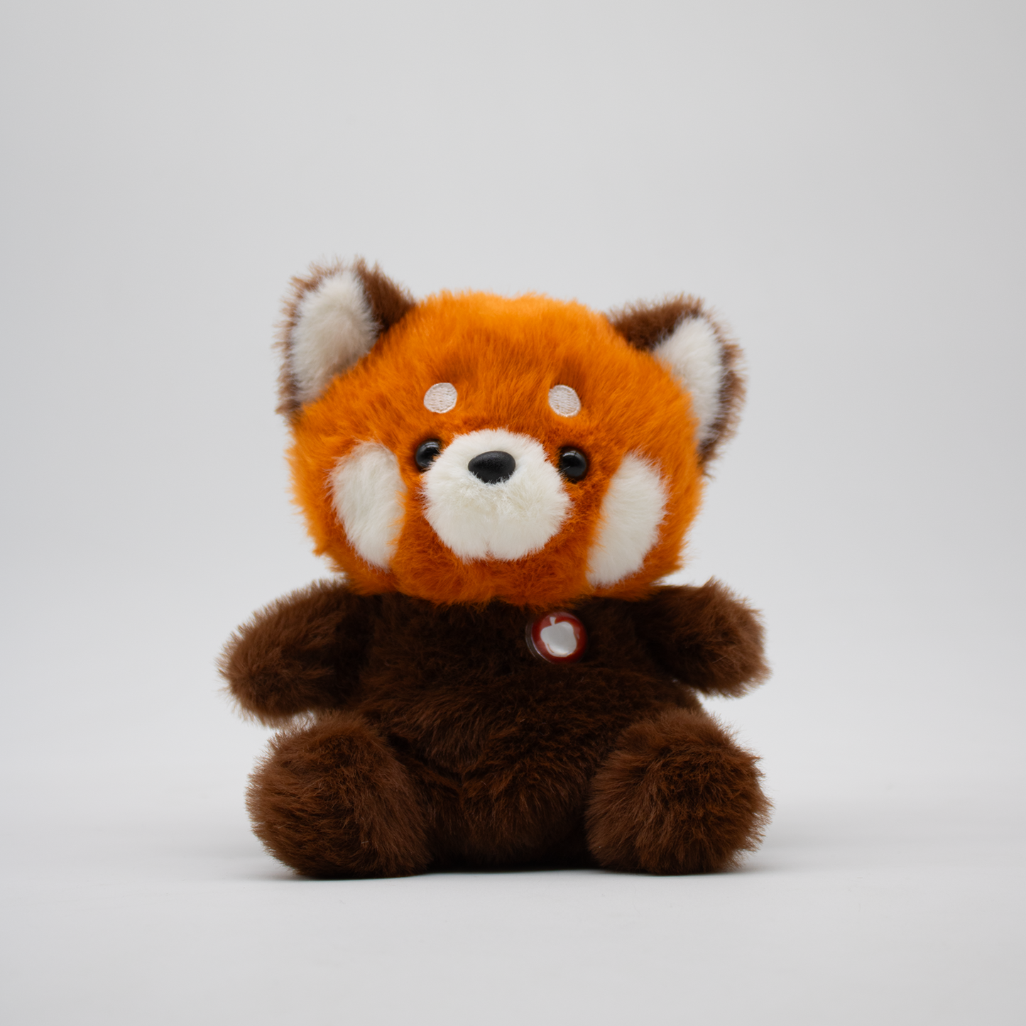 Stuffed red panda plush with an orange face and brown body on a white background