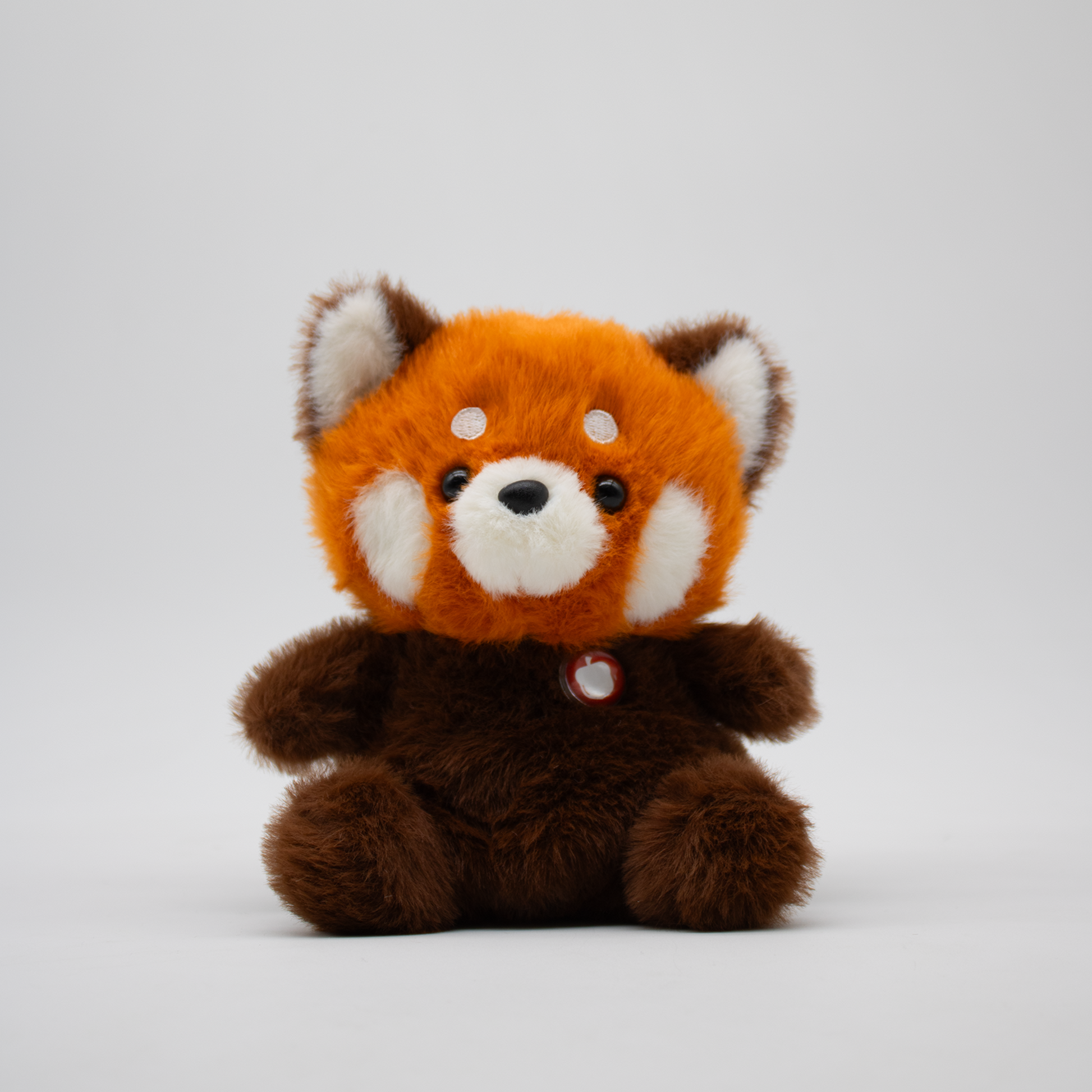 Stuffed red panda plush with an orange face and brown body on a white background
