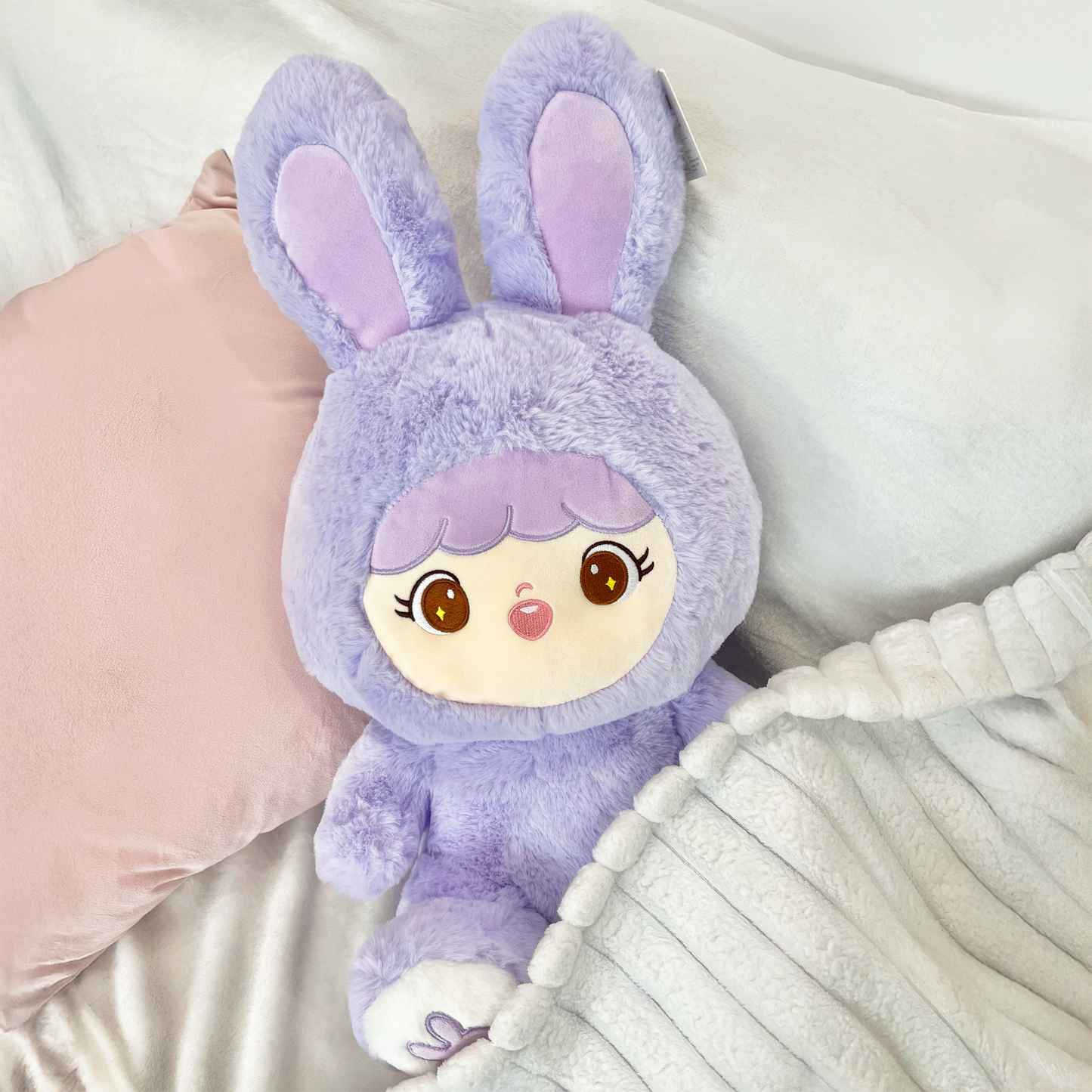 Shoobi in lifestyle setting slightly under blanket on a bed